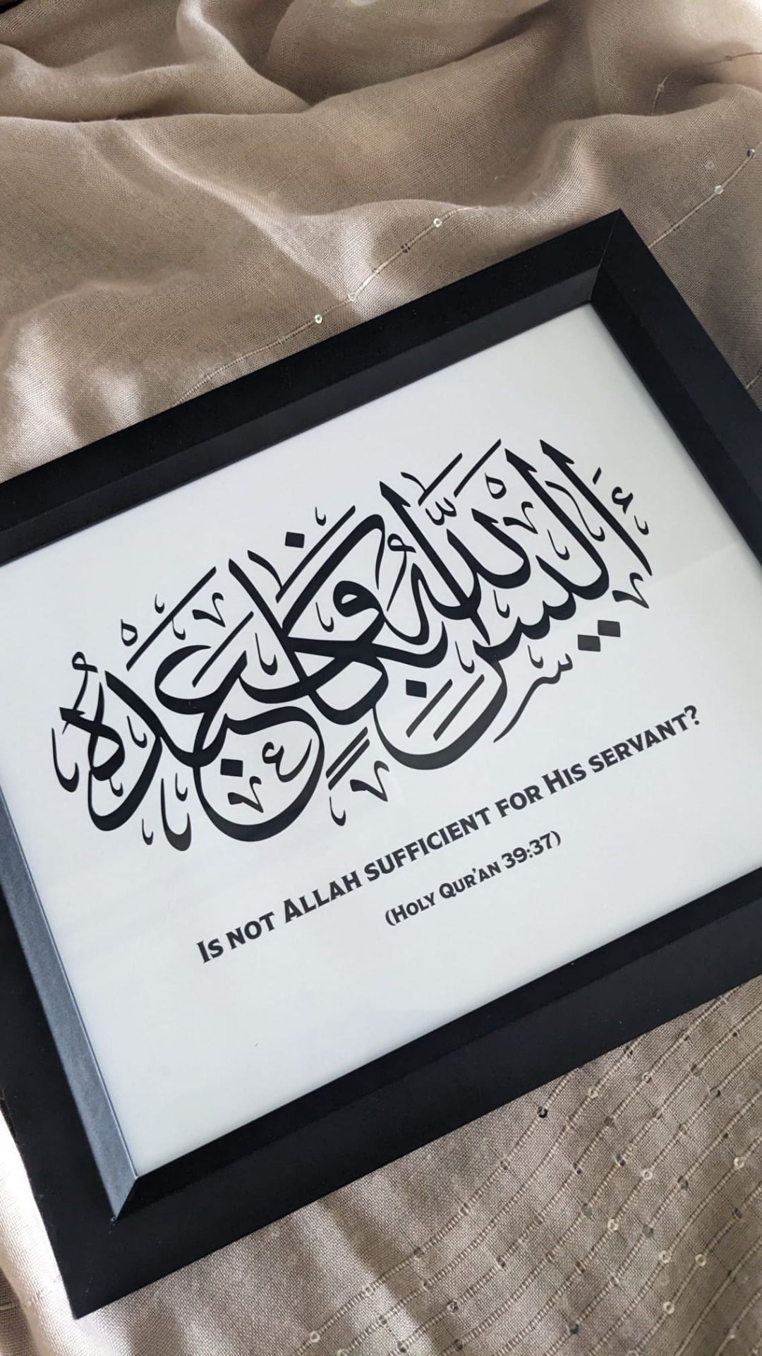 The same calligraphy in a black frame, photographed on a beige scarf